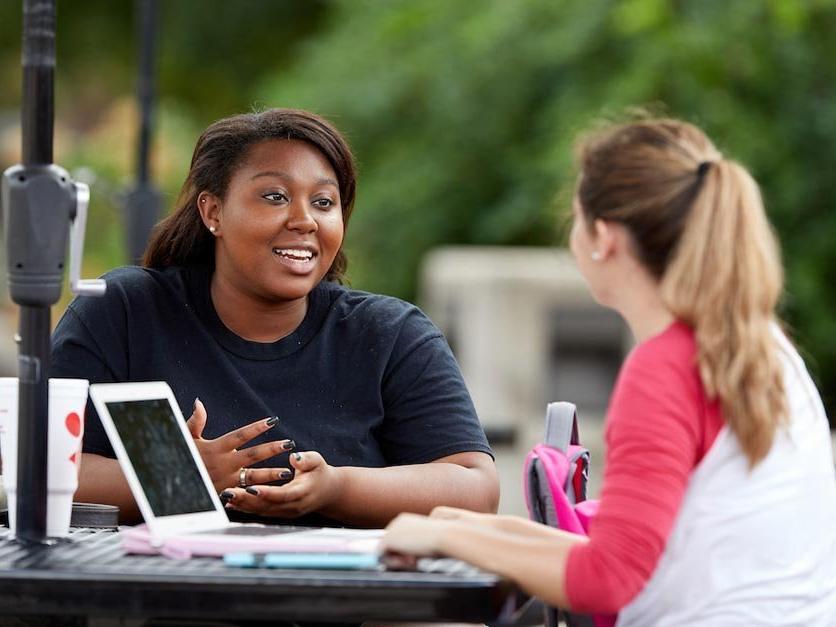 Two female students working outside on class assignment at table